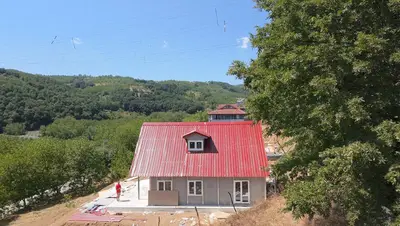 Çift katlı çelik ev, kırmızı çatı: cephe kolonları görünür, çatı makası kuruluyor — montaj ekibimizin saha fotoğrafı (2/3)
